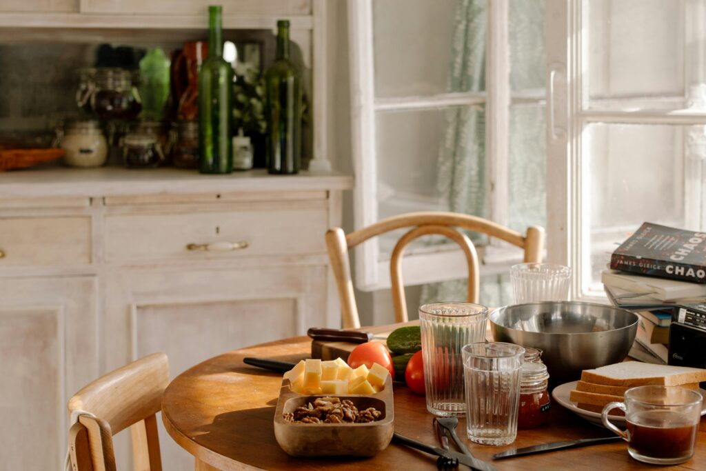 A sunlit kitchen table with food, glassware, and books, creating a warm, inviting ambiance.